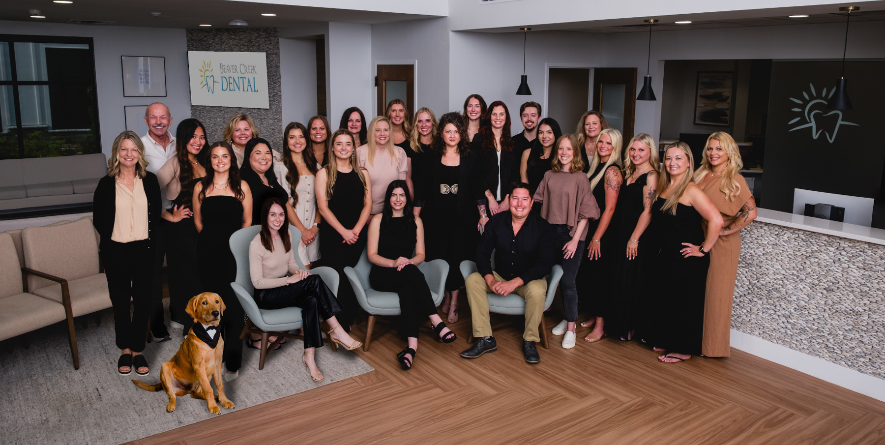 Beaver Creek Dental | Group photo of the Beaver Creek Dental team standing and seated together in the office lobby, with a golden retriever in a tuxedo sitting in front.